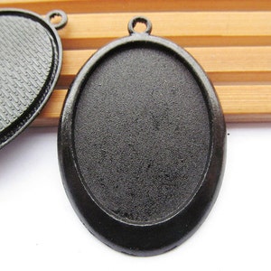 May include: Two black metal oval pendant trays with a textured surface. The trays are designed to hold a cameo or other decorative item.