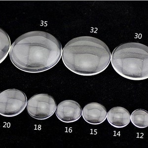 Peut inclure: Assortiment de cabochons en verre transparent de diff&eacute;rentes tailles, allant de 8 mm &agrave; 40 mm de diam&egrave;tre. Les cabochons sont dispos&eacute;s en deux rang&eacute;es, les plus grands en haut et les plus petits en bas.