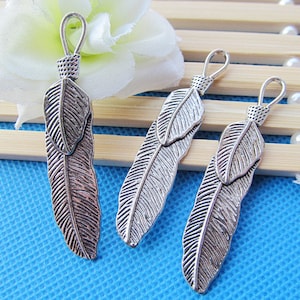 May include: Three silver feather charms with a loop at the top for attaching to jewelry or other crafts. The feathers are detailed with a textured surface and have a slightly oxidized finish.