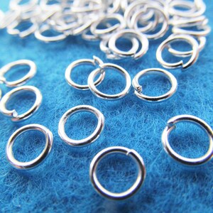 May include: A close-up of a pile of silver jump rings on a blue surface. The jump rings are small and round, and they are perfect for jewelry making.