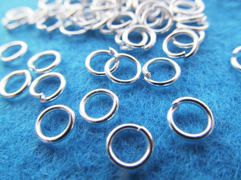 May include: A close-up of a pile of silver jump rings on a blue surface. The jump rings are small and round, and they are perfect for jewelry making.