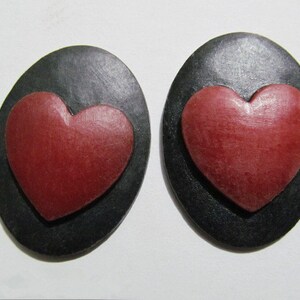 May include: A pair of black oval-shaped earrings with a red heart-shaped design in the center of each earring.