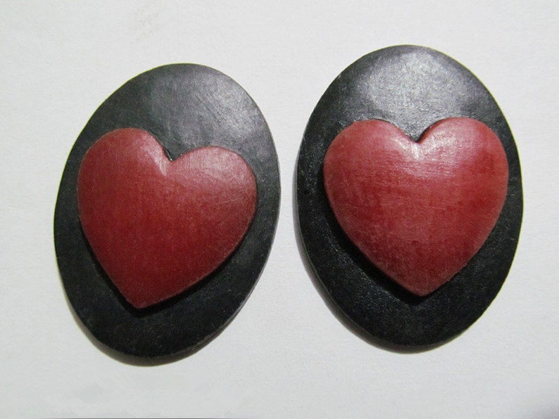 May include: A pair of black oval-shaped earrings with a red heart-shaped design in the center of each earring.