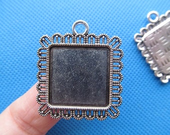 May include: Silver-toned metal frame with a square, clear glass insert. The frame has a decorative, scalloped edge and a loop at the top for hanging.
