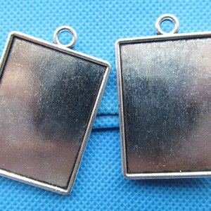 Puede incluir: Dos colgantes de marco de imagen de metal plateado con un bucle en la parte superior para colgar. Los marcos son rectangulares y tienen una superficie ligeramente texturizada.