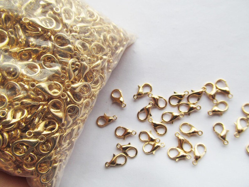 Puede incluir: Una bolsa de cierres de langosta de metal dorado, con algunos cierres esparcidos sobre una superficie blanca.