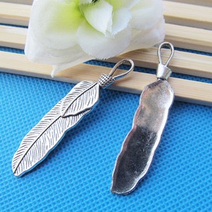 May include: Two silver-toned metal charms in the shape of feathers. One charm is a simple, flat feather, while the other is a more detailed, textured feather.