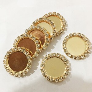 May include: Six gold-toned round metal embellishments with clear rhinestone borders. The embellishments have a smooth, reflective surface.
