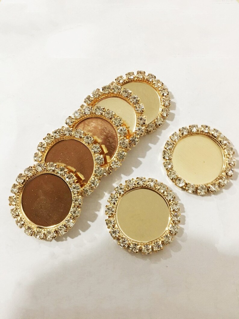 May include: Six gold-toned round metal embellishments with clear rhinestone borders. The embellishments have a smooth, reflective surface.