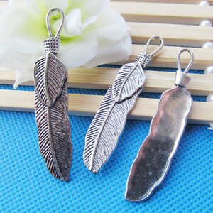 May include: Three silver feather charms with a loop at the top for attaching to jewelry or other crafts. The feathers have a detailed design and a rustic finish.