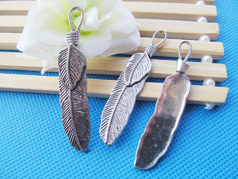 May include: Three silver feather charms with a loop at the top for attaching to jewelry or other crafts. The feathers have a detailed design and a rustic finish.
