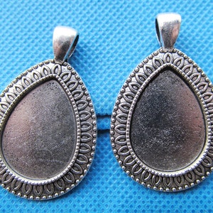 Könnte beinhalten: Zwei silberfarbene Anhänger-Tabletts mit Tropfenform und verziertem Rand. Die Tabletts sind leer und bereit zum Verzieren.