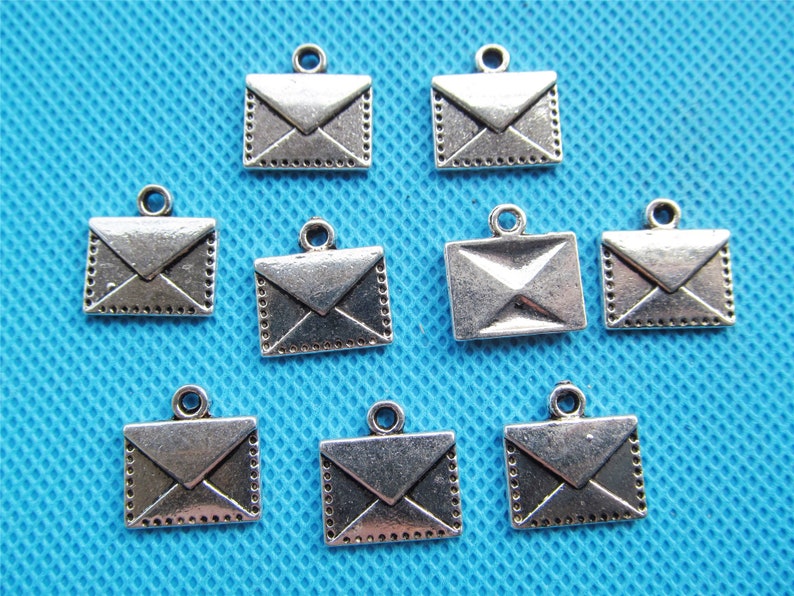 May include: Ten silver-toned metal envelope charms with a loop for hanging. The charms are about 1 inch in size and have a detailed design.