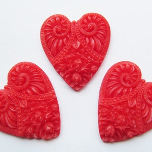 May include: Three red heart-shaped buttons with an intricate floral design. The buttons are made of a smooth, glossy material.