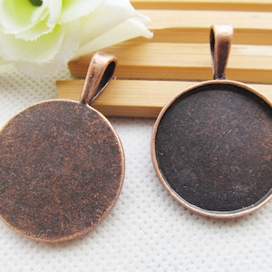 May include: Two round copper-toned metal pendant trays with a loop at the top for hanging. The trays are blank and ready for crafting.