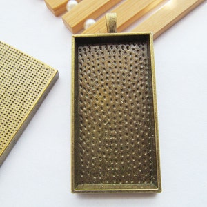Puede incluir: Una bandeja rectangular de metal con una superficie texturizada y un bucle para colgar. La bandeja está diseñada para contener una pequeña imagen u otro objeto decorativo.