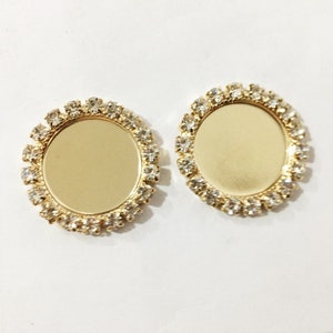 May include: Two gold-toned round metal frames with clear rhinestones around the edges. The frames are blank and can be used for crafting.