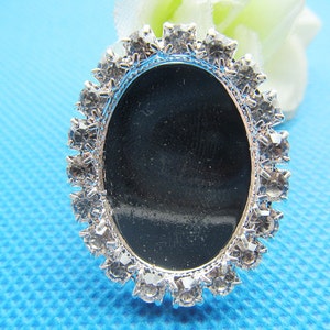 Puede incluir: Un marco ovalado plateado con fondo negro y un borde de pedrería transparente.