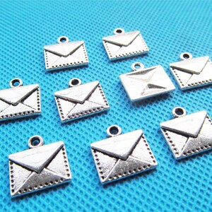 May include: Ten silver-toned metal envelope charms with a loop for hanging. The charms are about 1 inch in size and have a detailed design.