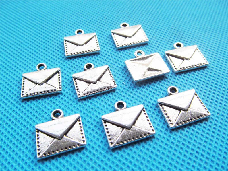 May include: Ten silver-toned metal envelope charms with a loop for hanging. The charms are about 1 inch in size and have a detailed design.