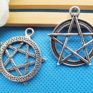 May include: Two silver-toned metal charms in the shape of a five-pointed star. The star on the left is enclosed in a circle with a textured surface. The star on the right is outlined with a circle.