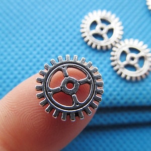 May include: Silver metal gear charms with a detailed design. The gears are small and have a shiny finish.