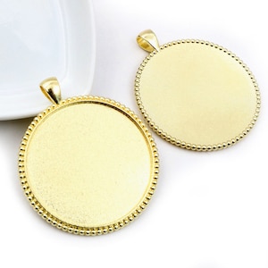 May include: Two gold-toned metal pendant trays with a beaded edge. The trays are round and have a smooth surface.