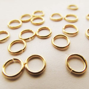 May include: A close-up of a group of gold jump rings. The rings are small and round, and they are all made of the same metal.