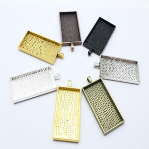 Peut inclure: Assortiment de six plateaux rectangulaires en métal pour pendentifs, dans différentes finitions, notamment or, argent, noir, bronze et cuivre. Chaque plateau a une surface texturée et une boucle pour attacher une chaîne ou un cordon.