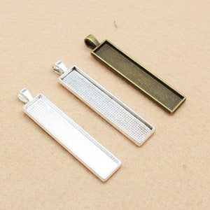 May include: Three rectangular pendant trays with a silver, antique silver, and gold finish. The trays are designed to hold small items like photos, charms, or other decorative elements.