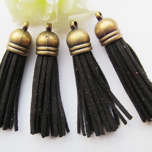 May include: Four black suede tassels with antique gold metal tops. The tassels are approximately 2 inches long.