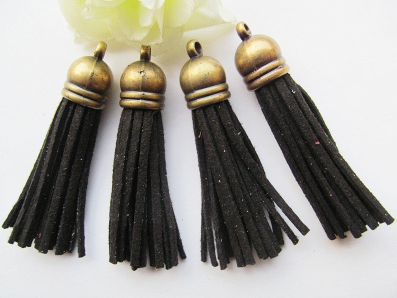 May include: Four black suede tassels with antique gold metal tops. The tassels are approximately 2 inches long.