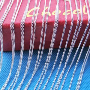 May include: A close-up image of a large quantity of silver chains, arranged in rows, on a red box with the word "Chocalat" printed on it. The chains are lying on a blue surface.