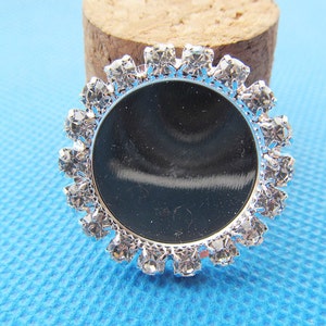 May include: Silver round bezel with a clear rhinestone border. The bezel is designed to hold a cameo or other small object.