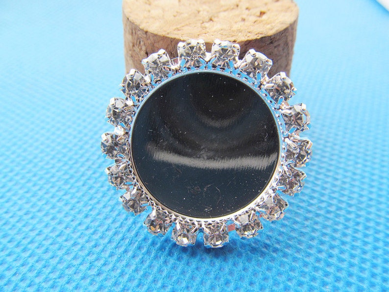 May include: Silver round bezel with a clear rhinestone border. The bezel is designed to hold a cameo or other small object.