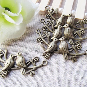 May include: A set of antique silver charm pendants featuring pairs of birds perched on branches. The charms are detailed with intricate designs and have a rustic, vintage aesthetic.