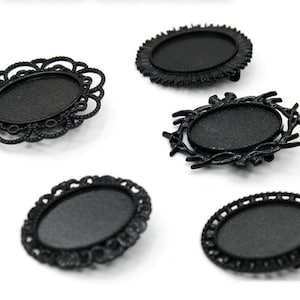 May include: Five black metal oval-shaped picture frames with different decorative borders. The frames are all empty and ready to be filled with photos or other artwork.