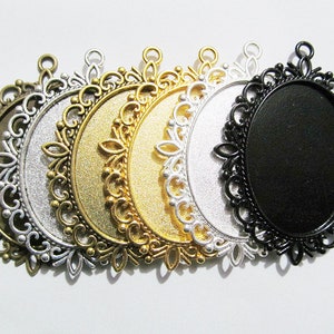Puede incluir: Seis bandejas ovaladas de metal para colgantes con diseños de filigrana ornamentados. Las bandejas son de plata, oro y negro.