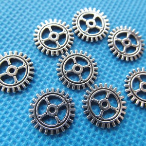 May include: Eight silver metal gears of varying sizes on a blue textured background.