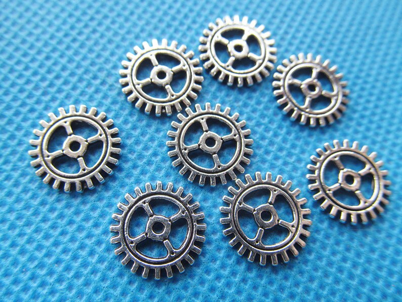 May include: Eight silver metal gears of varying sizes on a blue textured background.