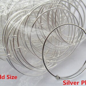 May include: A close-up of a pile of silver-plated, child-sized bangle bracelets. The bracelets are made of thin metal and have a simple, circular design. The text "Child Size" and "Silver Plated" is visible at the bottom of the image.