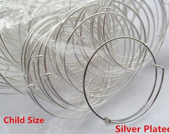 Puede incluir: Primer plano de una pila de pulseras de brazalete plateadas para niños. Las pulseras están hechas de metal delgado y tienen un diseño simple y circular. El texto "Child Size" y "Silver Plated" es visible en la parte inferior de la imagen.