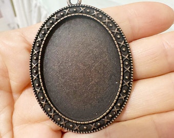 May include: An oval-shaped metal pendant with a decorative border. The pendant is made of a dark bronze-colored metal and has a smooth, polished finish.