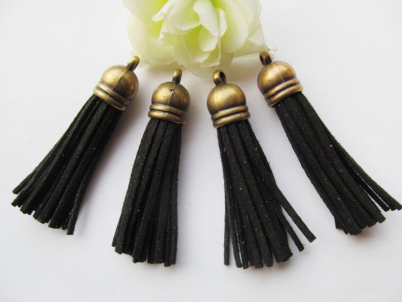 May include: Five black suede tassels with antique gold metal tops. The tassels are approximately 2 inches long.