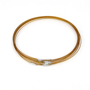 May include: A set of six gold-colored metal necklace chains with silver clasps. The chains are stacked on top of each other.