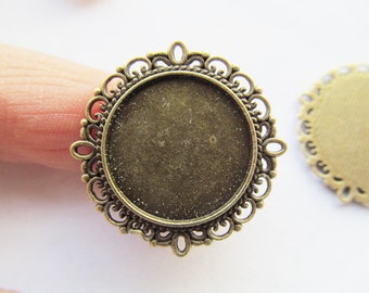 May include: A gold-toned metal ring setting with a decorative filigree design. The setting is designed to hold a round, flat-backed cabochon.