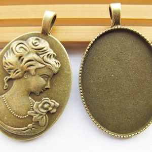 May include: Two antique gold-toned metal pendant trays. One tray features a raised design of a woman's profile with a rose. The other tray is blank.