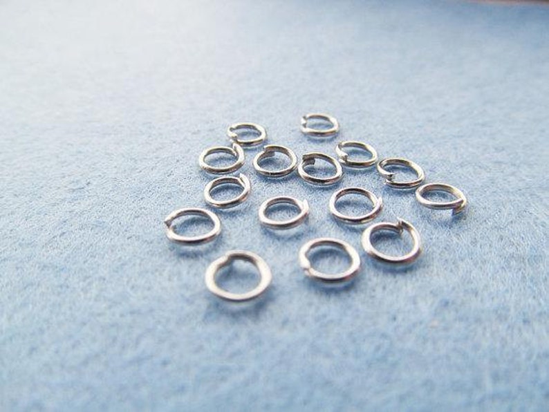 May include: A collection of silver jump rings, a type of jewelry finding, scattered on a light blue surface.