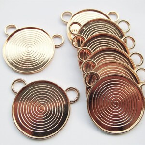 May include: A set of ten gold-toned metal pendant trays with a spiral design. Each tray has two jump rings for attaching to a necklace or bracelet.