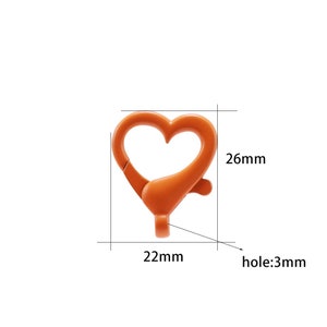 May include: Orange heart-shaped metal clasp with a 3 mm hole. The clasp measures 22 mm wide and 26 mm tall.